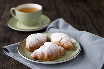 Freshly baked croissants cup with green tea on a brown wooden background.