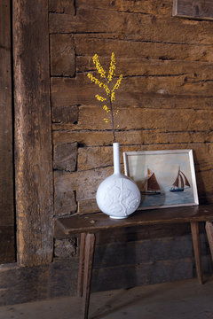 Blume in weisser Porzellan Vase vor Bild mit Segelbooten und alter Holzwand