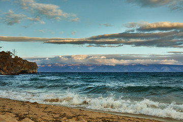 Azure beach with stony mountains and clear water of Baikal on a cloudy day.