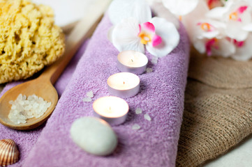 Spa scene - candles on the towel, salt, orchid, natural sponge, and stones in the arrangement