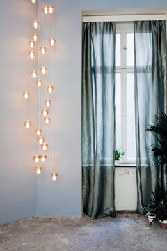 Grosse Hänge Lampe neben Fenster mit silbrig grünen transparent Vorhängen vor Fenster
