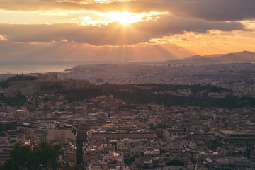 Fototapeta premium Beautiful sunset above Athens city and acropolis with sun rays light throw the clouds