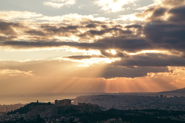 Beautiful sunset above Athens city and acropolis with sun rays light throw the clouds