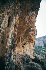 man climbs an overhang tufa cliff  like a cave in Greece