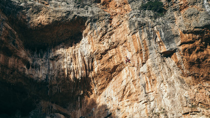 man climbs an overhang tufa cliff  like a cave in Greece