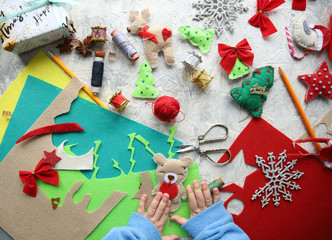 child sews New Year's felt toys. View from above