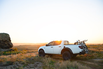 Fototapeta na wymiar Pickup Offroad Truck with Bikes in the Body in the Mountains at Sunset. Adventure and Car Travel Concept.