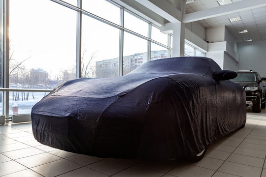 Sports car in a motor show, carefully prepared for winter storage, covered with a professional cover made of blue special fabric, custom-made, perfectly suitable for all parts of the body surface.