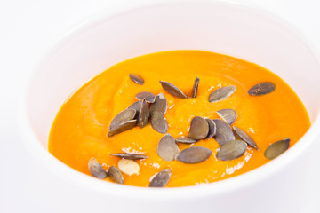 Pumpkin soup decorated with pumpkin seeds in a bowl on a white background