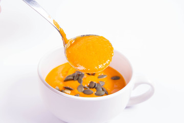 Pumpkin soup decorated with pumpkin seeds in a bowl on a white background