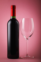 Bottle of red wine and an empty wine glass close-up on pink background. Still life with alcohol