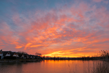 Beautiful sunset at Lake Neusiedlersee in Austria with colorful orange and red illuminated cloudy sky. Picturesque holiday homes in terraced settlement. Reed grows on the shore.