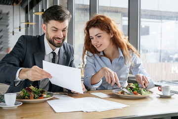 Businesspeople having business lunch at restaurant sitting eating man showing woman document...