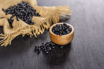 Lot of whole raw black turtle beans jute cloth with wooden bowl on grey stone