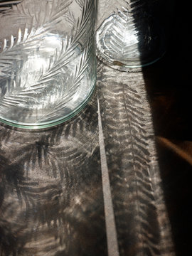 Zwei Glas Vasen mit gefr&auml;stem Muster werfen Schattenmuster auf Steinboden