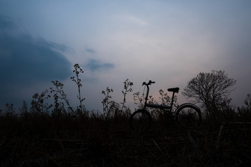 Silhouette of bicycle in dry grass field on looking at sunset on the mountain. in the sunset.