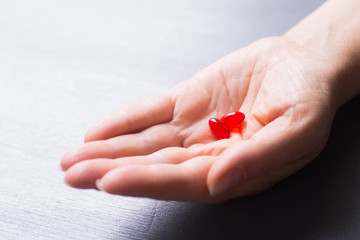 Caucasian female hand holding two transparent red capsules on table