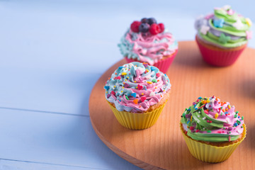 Closeup different colorful cupcakes decorated with sprinkles on wooden round desk.