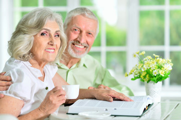 Portrait of happy senior couple sitting at table and reading book