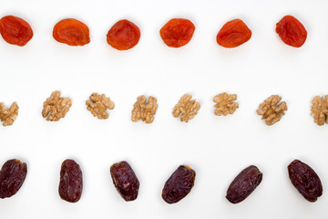 Rows of dates, dried apricots and walnuts on the white background. Top view, flat lay, copy space, pattern