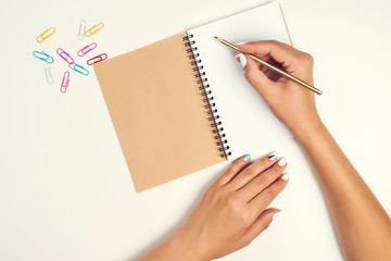 Female hand with pencil. White sheet of paper on desk. Notebook. Top view of work desk. Mockup for your design. Flay lay, office desk. Feminine desk workspace. Ideas, notes or plan writing concept