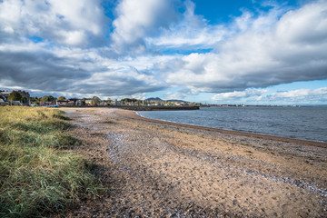 Empty Sandy Beach on the Coast of Scotland under Blue Sky with Clouds in Autumn. A Seaside Town is Visible in Background.