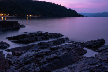 Sunset beautiful scene on a large black rock and there are lights from the beach resort. with beautiful sea at Koh Wai island, Trat province, Thailand
