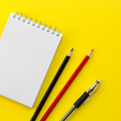 Notebook, black and red pencils, pen on the yellow background. Workspace concept. Flat lay, top view, copy space, mock up, square layout design