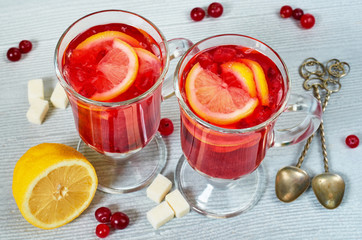 Hot winter healthy drink - cranberry tea or sangria with fresh lemon slices in glasses on the gray concrete kitchen background