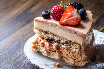 a piece of homemade cake with macaron and fresh fruit, berries on a white plate on a wooden background
