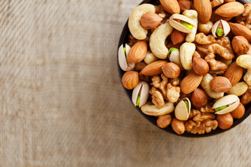 Mix of different nuts in a wooden cup against the background of fabric from burlap. Nuts as structure and background, macro. Top view.