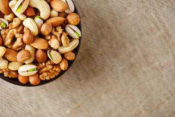 Mix of different nuts in a wooden cup against the background of fabric from burlap. Nuts as structure and background, macro. Top view.