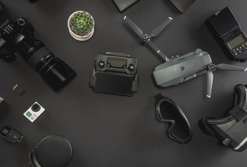 Work space photographer with laptop, digital camera, memory card, action camera, drone, remote controller, phone, VR glasses and camera accessory. Top view on black table background. 
