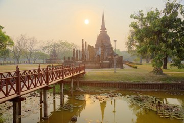 Sunset scenery of Wat Sa Si in Sukhothai Historical Park with the setting sun in background, a wooden bridge in foreground and the majestic temple in the middle ~ A beautiful heritage site in Thailand