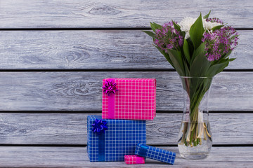 Vase with fresh flowers and gift boxes. Beautiful flowers and present boxes on vintage wooden background. Happy Mothers Day background.