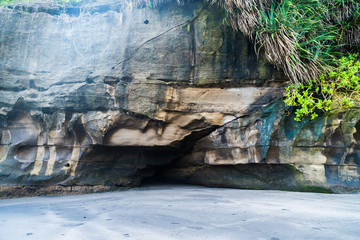 a small cave in the rock above the sandy beach