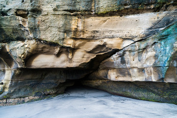 a small cave in the rock above the sandy beach