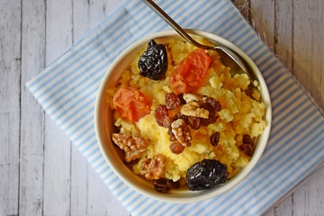 Useful porridge of corn grits and dried fruits on a wooden background.