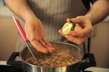 The chef adds lime to the soup tom yam. Hands of the cook close