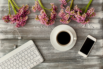 Top view of a keyboard, headphones and a cup of coffee, phone and a purple flower on a gray wooden table. Flat design.