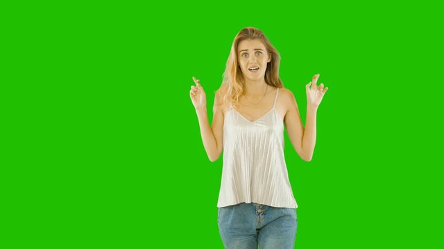 Pretty young woman with freckles crossed her fingers on both hands and raised her hands up expressing pity and surprise on her face, fashion shooting on an isolated background