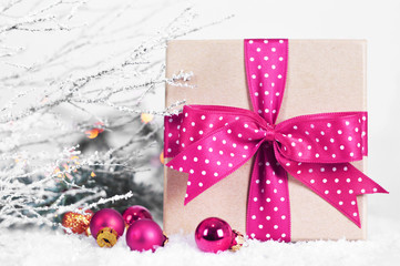 Fototapeta na wymiar Christmas gift with pink bow on snowy background