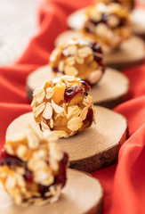 Handmade energy balls are lying diagonally in row on wooden saw cuts on red fabric.