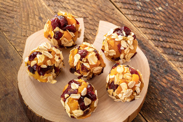 Six homemade energy balls are lying on wooden saw cut on brown wooden table.