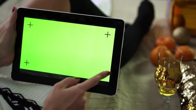 Woman holding tablet with blank green display on Christmas background.