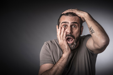 Fototapeta premium portrait of a 50 year old caucasian man with long hair and beard, hands on his head, surprised and amazed expression.
