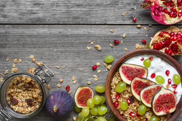 bowl of oat granola with yogurt, pomegranate seeds, figs, grape and nuts on rustic wooden background
