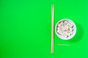 dice in a white bowl with chopsticks on a green background