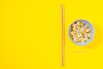 dice in white bowl with chopsticks on yellow background