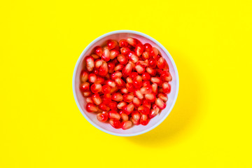 pomegranate seeds in a white bowl on a yellow background